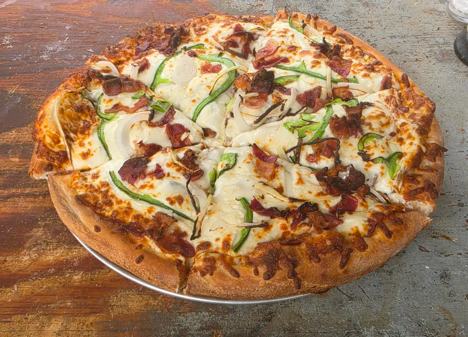 Pizza garnie de bacon, de lanières de poivron vert et d'oignon sur fromage gratiné, sur une plaque en aluminium