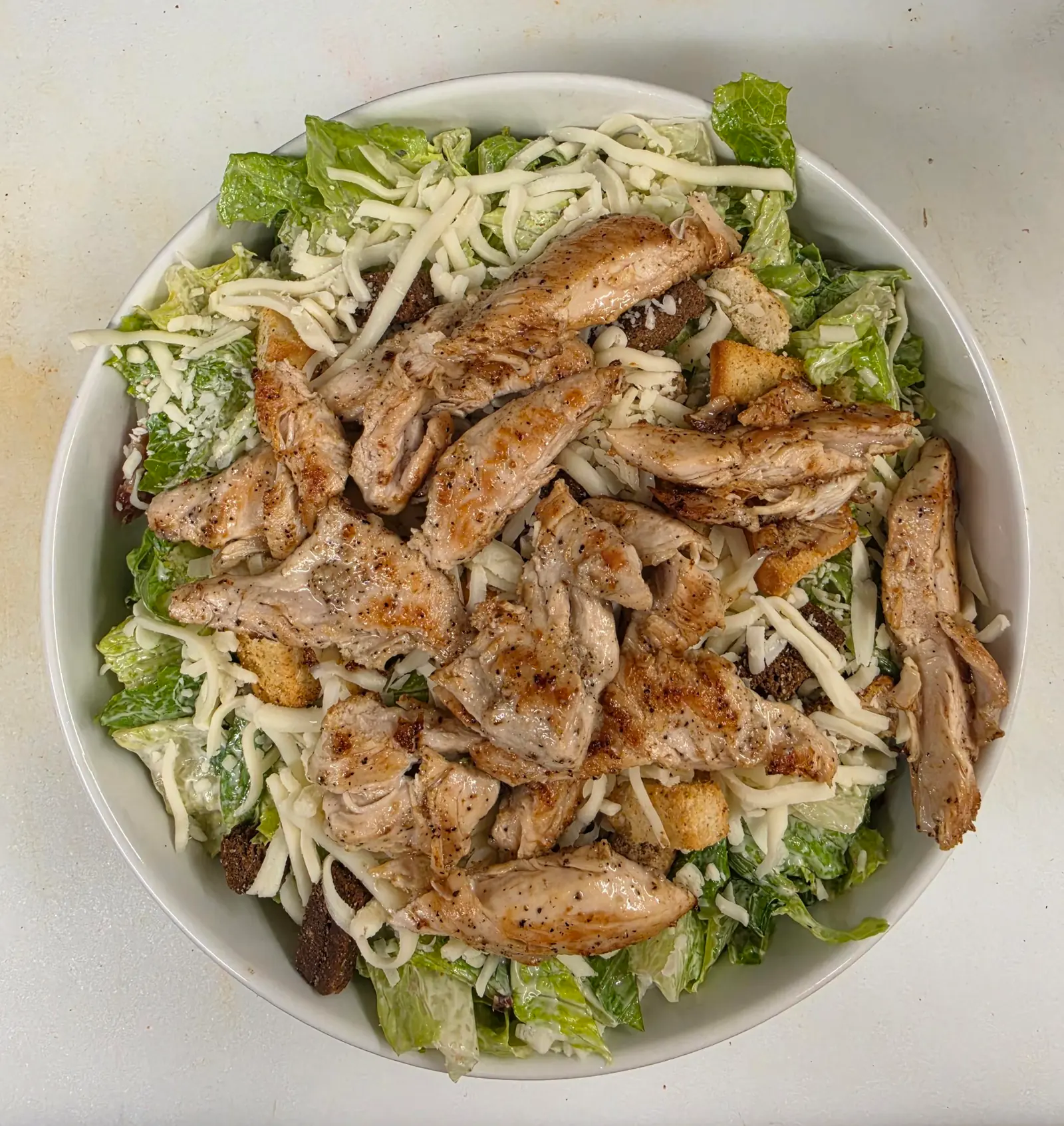 Bol de laitue romaine garni de lanières de poulet grillé, de fromage râpé et de croûtons, vu de dessus
